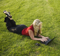 A woman lying on a lawn using her notebook computer